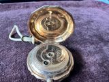 une montre de poche en argent posée sur une couverture violette