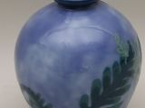 a blue vase with green leaves on it on a white surface