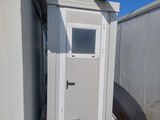 une toilette extérieure blanche avec une porte sur le côté du bâtiment