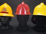 three firemen hats on mannequin heads against a black background