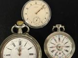 trois montres de poche différentes posées sur une surface noire