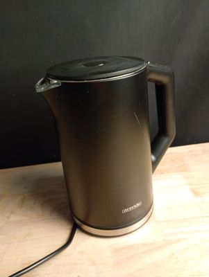 a black kettle sitting on a wooden table with a black wall in the background