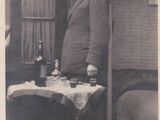 an old black and white photo of a man standing in front of a table with a bottle of wine on it