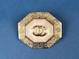 an image of a gold and white broochle on a blue surface