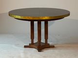 une petite table ronde au plateau doré, posée sur un sol blanc