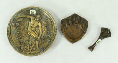 une plaque en bronze et une cuillère en bois posées sur une surface blanche