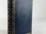 a blue book with gold trim and a black cover on a white surface