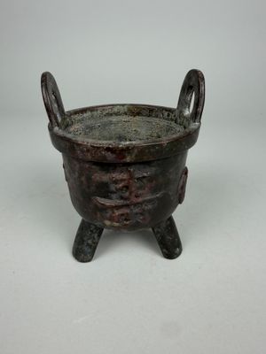 an old bronze pot with two legs on a white surface