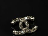 a chanel broocher made of silver metal with a black background