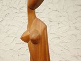 wooden sculpture of a woman with a hat on her head, standing against a white wall