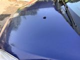 a blue car that has a bullet stuck in the hood