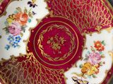 a red and gold plate with flowers on it next to a cup and saucer