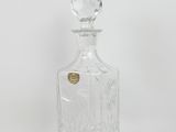 a clear glass bottle with a gold stopper sitting on a white surface