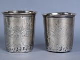 two silver cups with designs on them sitting on a table