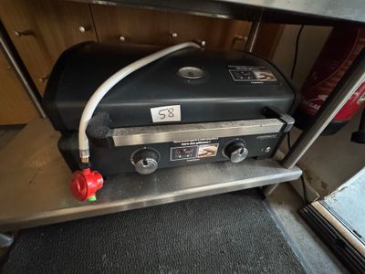 un barbecue à gaz posé sur une étagère métallique près d'une fenêtre