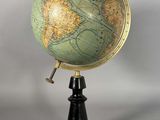 un globe vert et or posé sur un socle noir, sur fond blanc