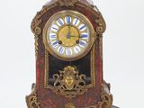a red and gold clock sitting on a white surface