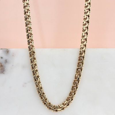 une photo d'un collier à chaîne en or posé sur une surface en marbre