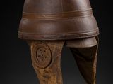 un casque en cuir marron posé sur un socle, sur fond noir