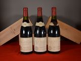 Trois bouteilles de vin sont posées sur une nappe rouge, avec une caisse en bois en arrière-plan.