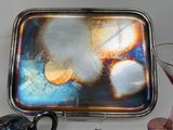 a silver tray with a painting on it next to a wine glass