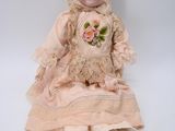 an old doll with a pink dress and brown shoes sitting on a white surface
