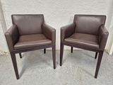 une paire de fauteuils en cuir marron posés sur un sol en béton, près d'un mur blanc
