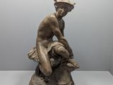 statue en bronze représentant un garçon assis sur un rocher, coiffé d'un chapeau
