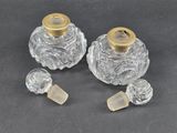two clear glass perfume bottles with gold caps on a black surface