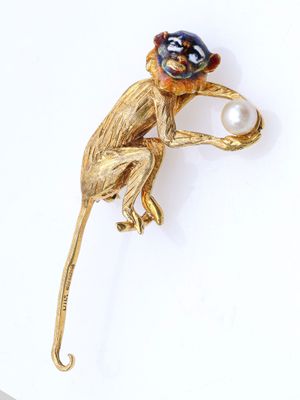 une image représentant une broche en forme de singe tenant une perle dans la bouche