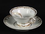 a white cup and saucer with a gold decoration on it