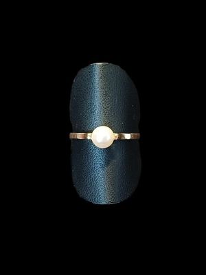 un gros plan d'une bague sertie d'une perle, posée sur une surface noire