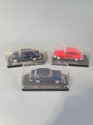 three miniature cars in plastic cases sitting on a white surface