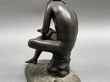 bronze statue of a man sitting on a rock with his legs crossed