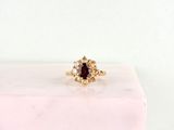un gros plan d'une bague en or sertie d'une pierre rouge entourée de petits diamants blancs