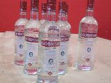 Six bouteilles de vodka Sobbie sont posées sur une table devant un mur rouge.