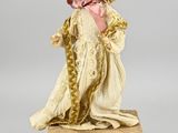 une poupée ancienne représentant une femme vêtue d'une robe blanche et d'un bonnet, tenant une rose