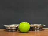 a green apple sitting next to two silver bowls on a table