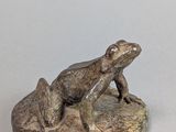 statue d'une grenouille assise sur un rocher, posée sur une surface blanche