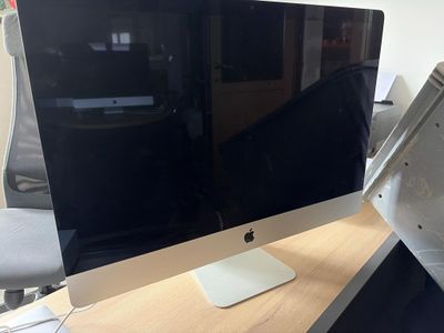 un ordinateur Apple posé sur un bureau en bois, à côté d'un écran d'ordinateur
