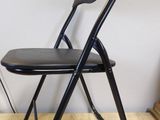 a black folding chair with a black seat on a wooden floor