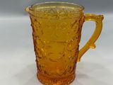 a close up of a yellow glass pitcher on a white surface