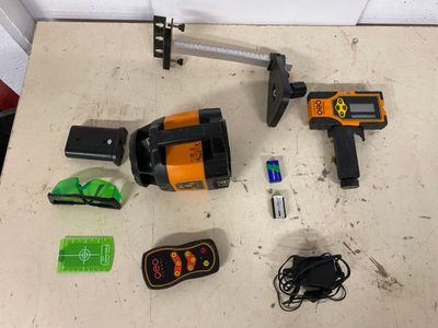 tools laid out on a table including a laser level, a hammer, a battery, a charger, and a corded cord
