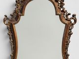 Un miroir richement sculpté est accroché au mur d'une pièce blanche.