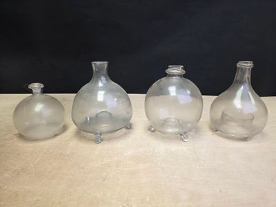 four glass vases sitting on a table with a black background