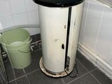 a water heater in the corner of a bathroom next to a trash can