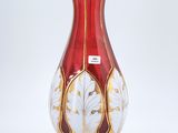 un vase rouge et doré posé sur une surface blanche