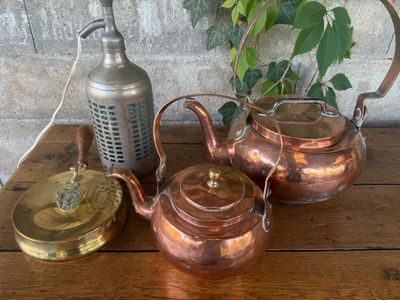 three copper kettles on a wooden table next to a teapot