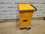 a yellow machine sitting on top of a cement floor next to a wall
