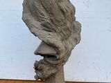 sculpture représentant une tête d'homme posée sur une table en bois, avec un mur blanc en arrière-plan